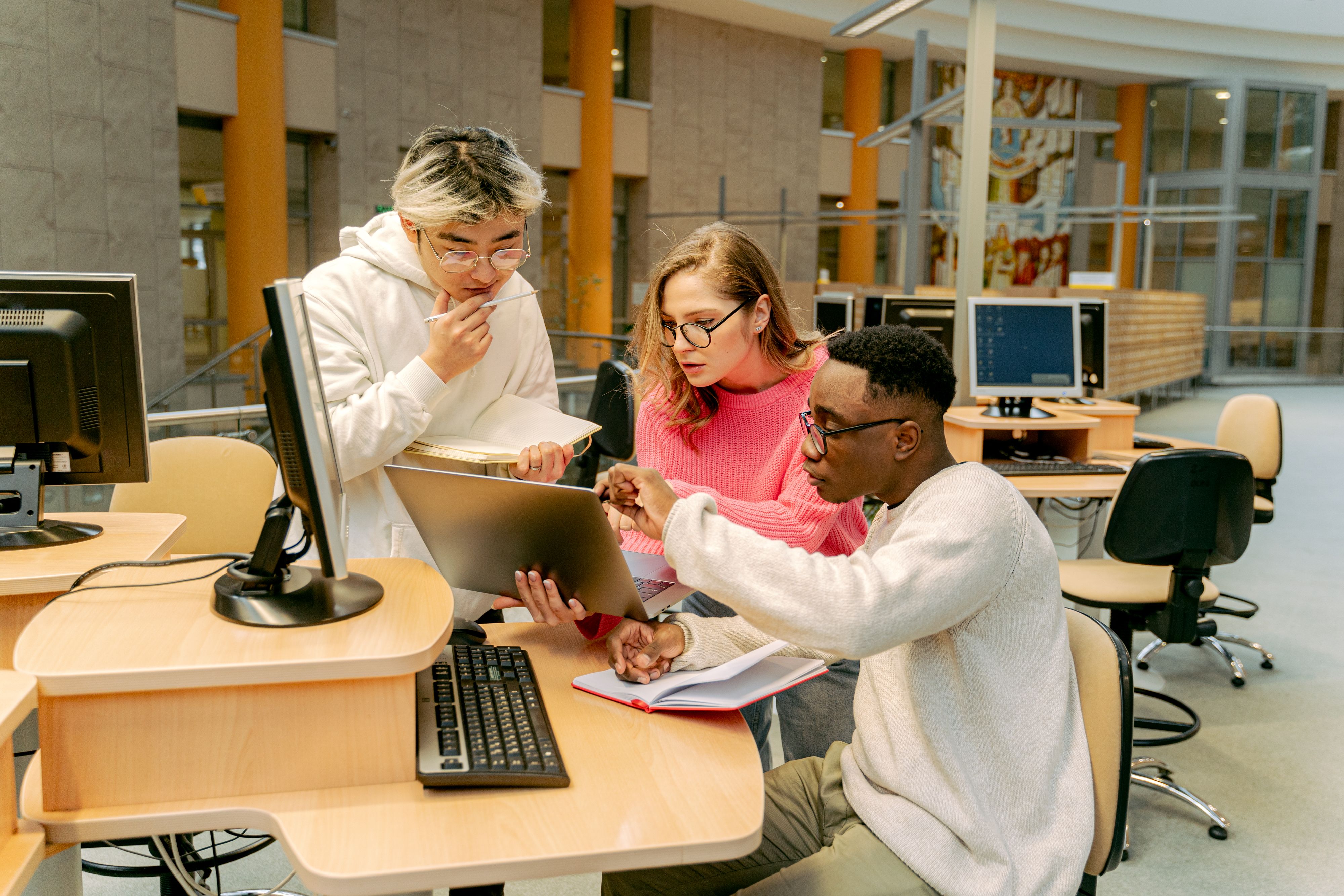 Adult students collaborating at computer workstations in a training lab.