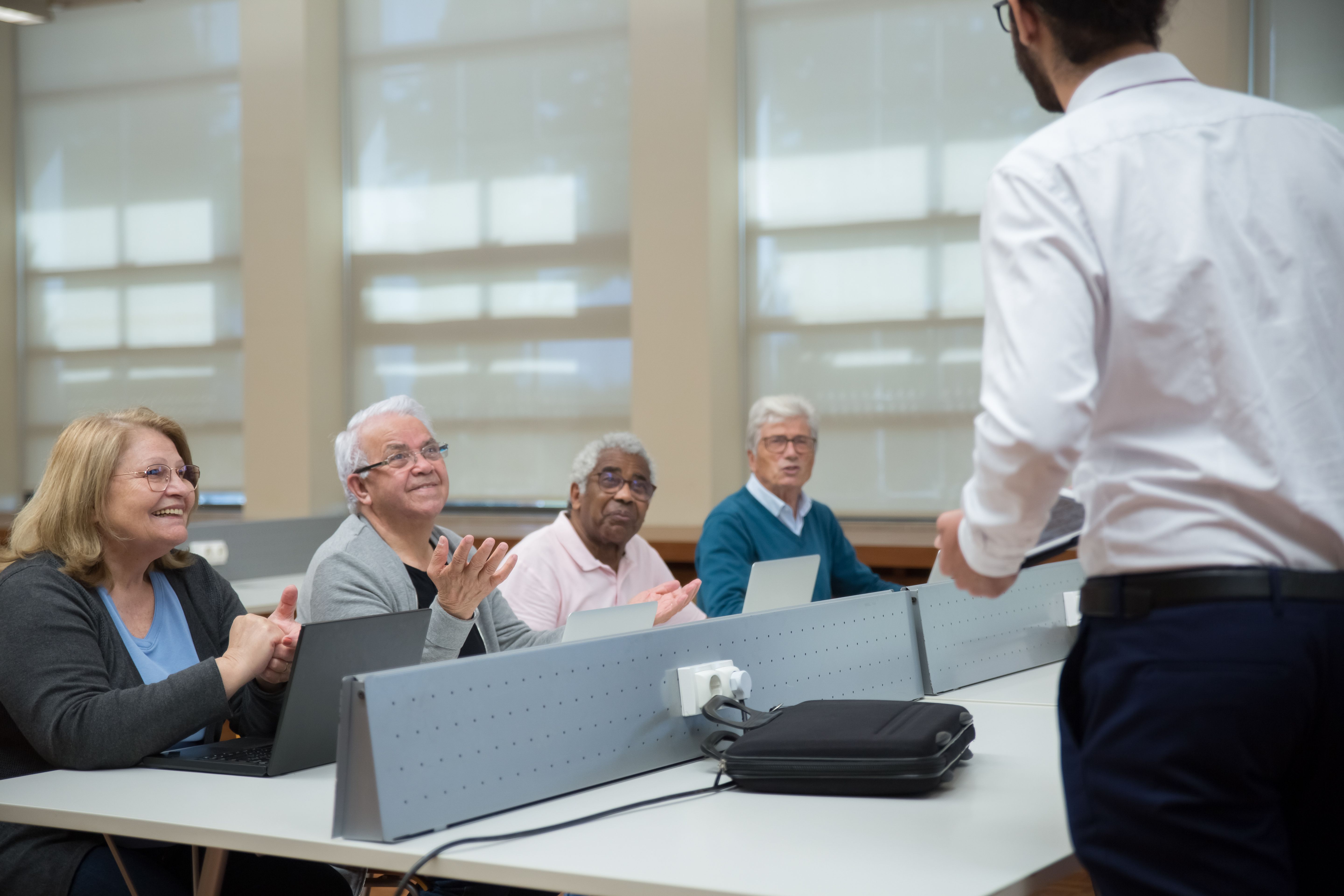 Older adults smiling in a warm technology classroom with an instructor.